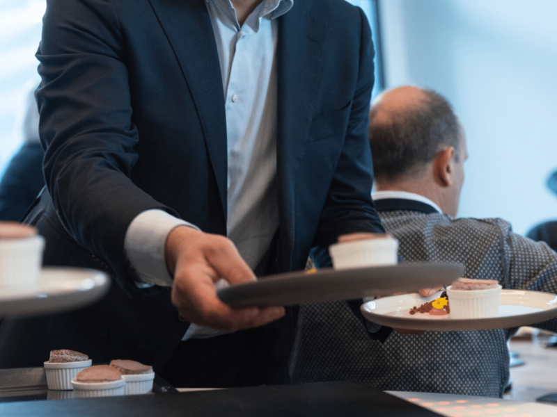 Waiter serving dessert to a room full of people