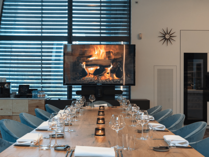 Meeting room with wooden table, fire place on the tv screen, cutlery, glasses and a candle on the table